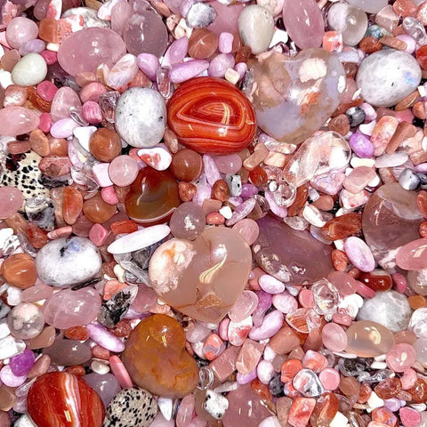 A vibrant mix of polished pink, white, and orange crystals, including heart-shaped stones, resembling confetti.