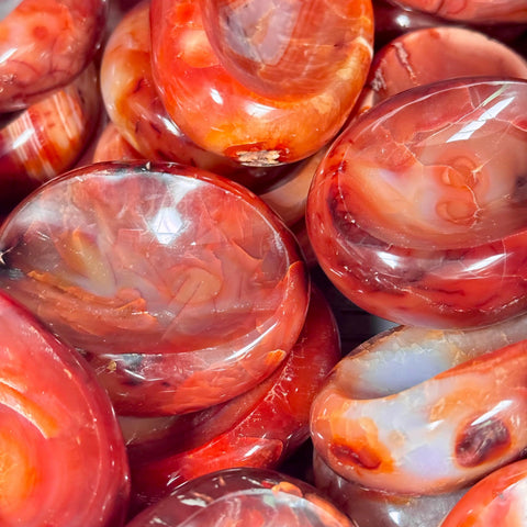 Polished, vibrant red carnelian stone bowls with smooth, glossy surfaces and natural banded patterns.
