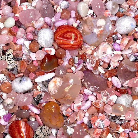 A vibrant mix of polished pink, white, and orange crystals, including heart-shaped stones, resembling confetti.