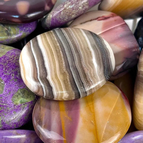 Polished palm stones in vibrant shades of purple, yellow, and banded brown agate.