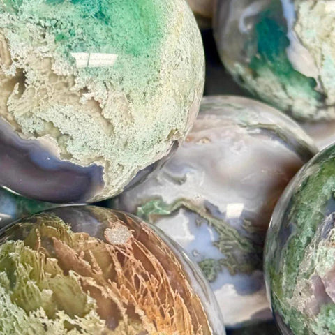 Polished moss agate spheres in varied green, white, brown, and purple hues with natural patterns.