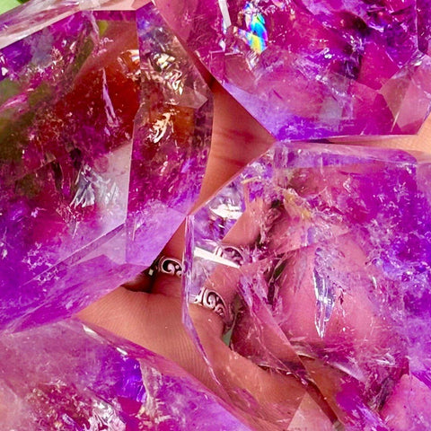 Close-up of vibrant purple amethyst crystals held in a hand, showcasing faceted edges and iridescent light reflections.