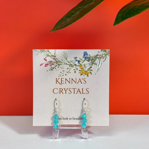Dangling Amazonite earrings with three light blue beads on silver hooks, displayed on a floral Kenna's Crystals card.