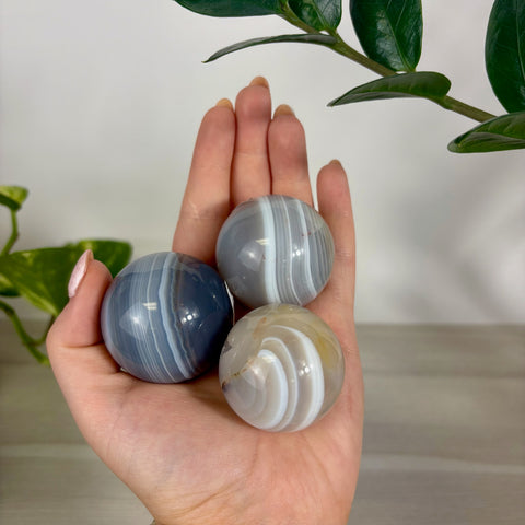 Three polished banded agate spheres in shades of blue, grey, and cream held in a palm.