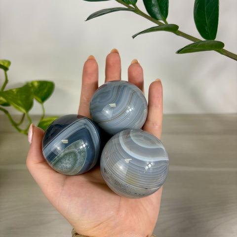 Three polished banded agate spheres with grey, blue, and white swirling patterns held in a palm.