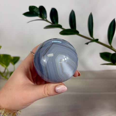 Polished blue banded agate sphere held in a hand, featuring natural grey and white geometric stone patterns.