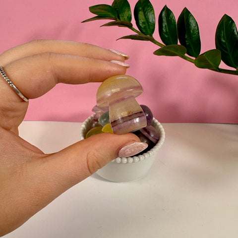 Hand holding a small, polished candy fluorite mushroom carving with yellow and purple banded crystal layers.