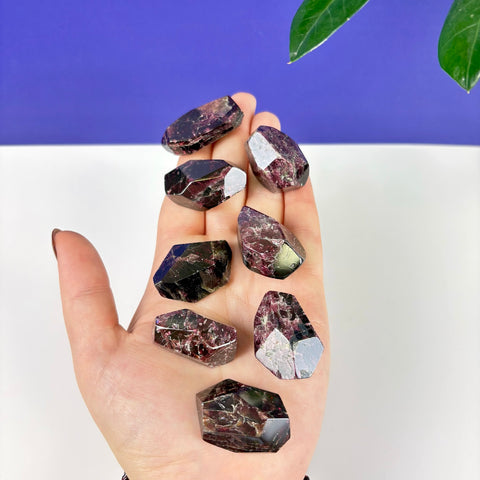 Hand holding several polished, deep red Cherry Blood Garnet crystal points with faceted surfaces.