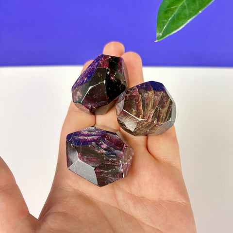 Three faceted, deep red garnet crystals with dark, cherry-toned inclusions held in a palm.