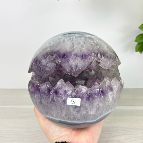 Polished amethyst and agate sphere with a jagged, crystalline open mouth design held in a hand.