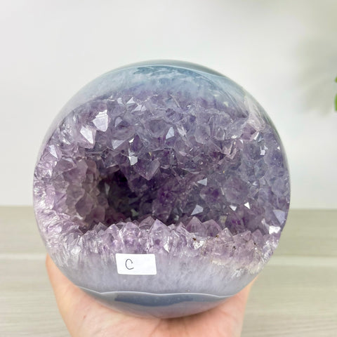 Polished amethyst geode sphere with a deep purple crystal center and smooth banded agate outer shell.