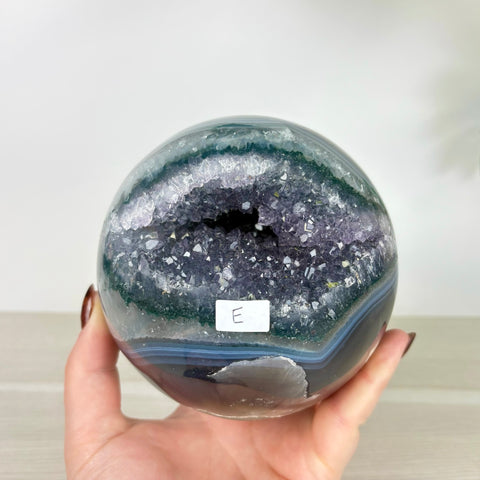 Polished amethyst and agate geode sphere with a deep purple crystal center held in a hand.