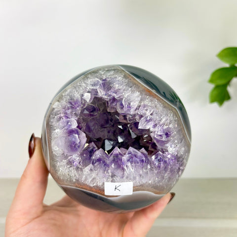 Polished agate sphere with a deep purple amethyst crystal geode center held in a hand.