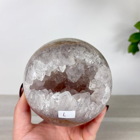 Large amethyst and agate geode sphere with a sparkling, jagged crystal-lined hollow center held in a hand.