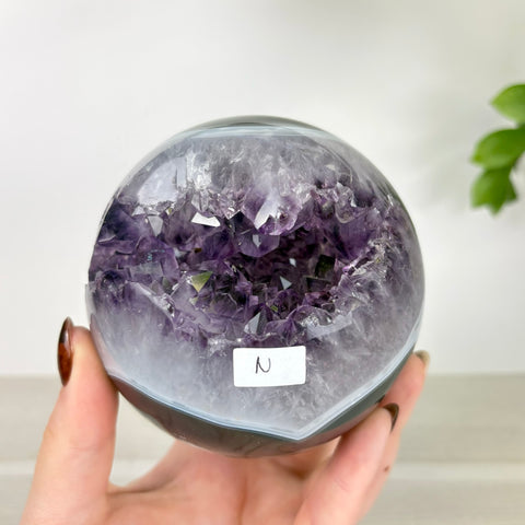 Polished amethyst and agate sphere with a deep purple crystal geode center held in a hand.