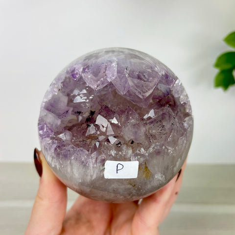 Polished amethyst geode sphere with a hollow crystal center held in a hand.