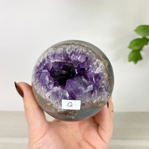 Polished amethyst and agate sphere with a deep purple crystal geode center held in a hand.