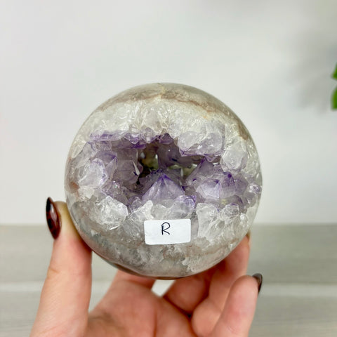 Handheld amethyst and agate chomp ball sphere featuring a deep purple crystal geode center and smooth stone exterior.