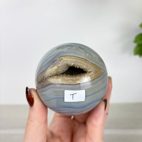 Polished blue agate sphere with a central crystalline geode opening held in a hand.