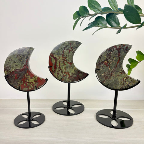 Three polished Dragon's Blood jasper moon carvings displayed on black metal stands against a white background.