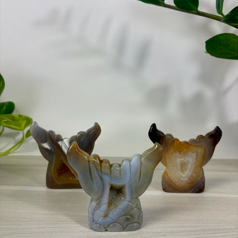 Three carved druzy agate mermaid tail sculptures in shades of grey, brown, and amber on a wooden surface.