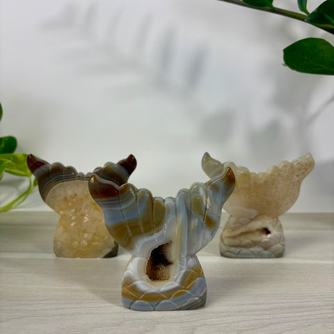 Three carved druzy agate mermaid tail sculptures with banded patterns and crystal centers on a wooden surface.