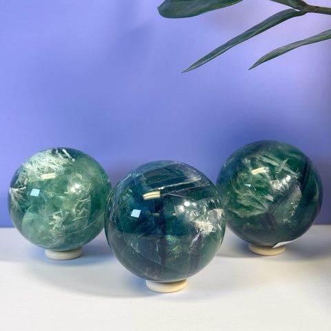 Three polished Feather Fluorite spheres in varying shades of green, with white inclusions, on a white surface.