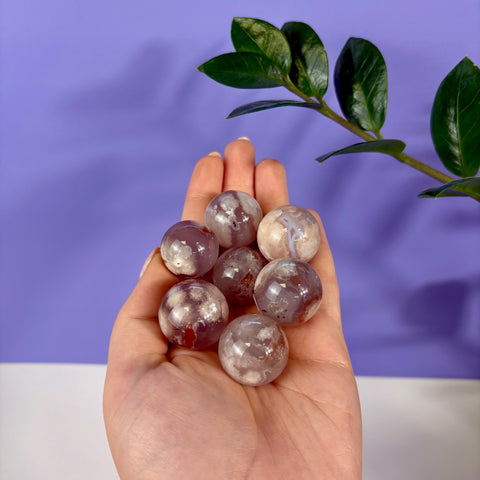 Hand holding seven small, polished flower agate spheres with pink, white, and translucent floral patterns.