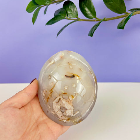 Polished druzy agate turtle shell carving with translucent gray tones and intricate crystalline inclusions held in hand.