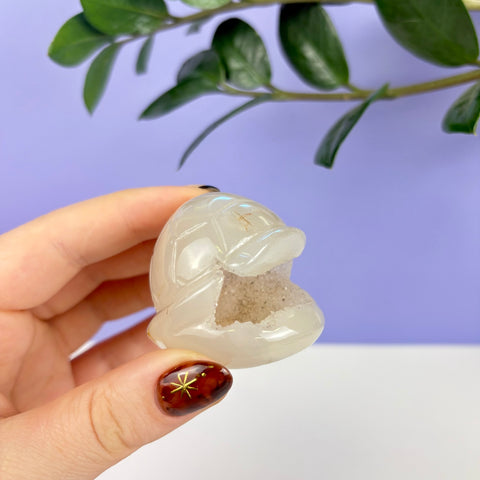 Handheld white druzy agate carved into a flying turtle shell shape with a sparkling crystalline center.
