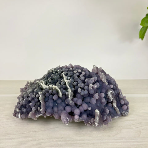 Deep purple grape agate cluster with botryoidal formations and white mineral inclusions on a light wooden surface.