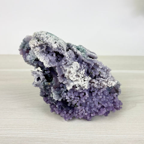 Grape agate cluster featuring vibrant purple botryoidal crystal spheres and white mineral formations on a light wood surface.