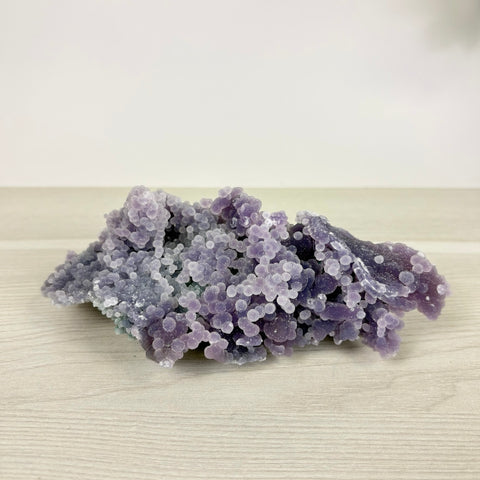 Deep purple grape agate cluster featuring sparkling, spherical botryoidal crystal formations on a light wooden surface.