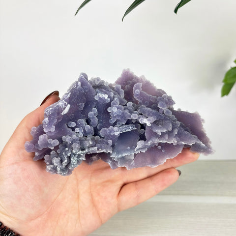Handheld cluster of deep purple grape agate with botryoidal, spherical crystal formations and a translucent, sugary texture.