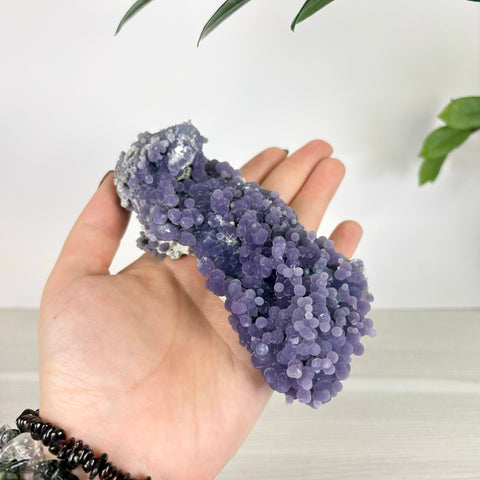 Hand holding a cluster of deep purple grape agate with small, spherical botryoidal crystal formations.