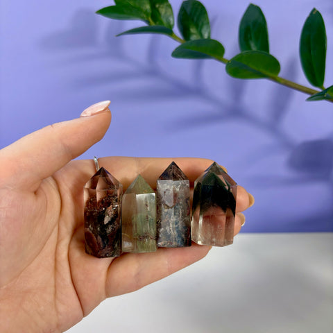 Four small Garden Quartz towers with unique mossy inclusions held in a hand against a purple background.