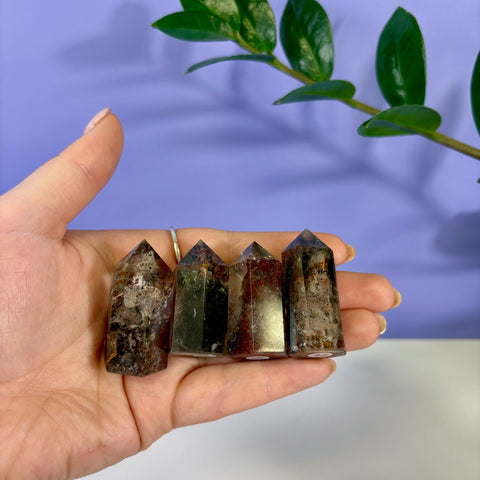 Four small Garden Quartz towers with earthy green and brown inclusions held in a palm against a purple background.