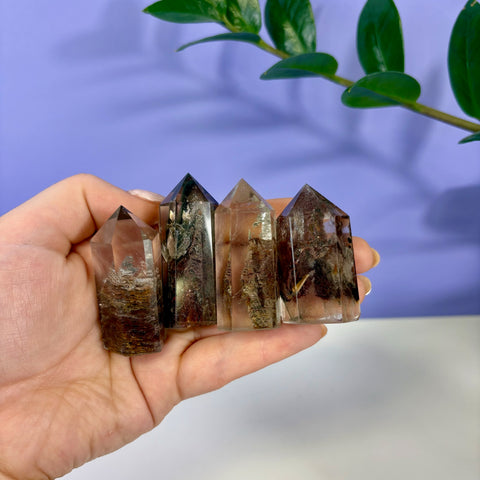 Hand holding four polished Garden Quartz towers with natural brown and green mineral inclusions inside clear crystal.
