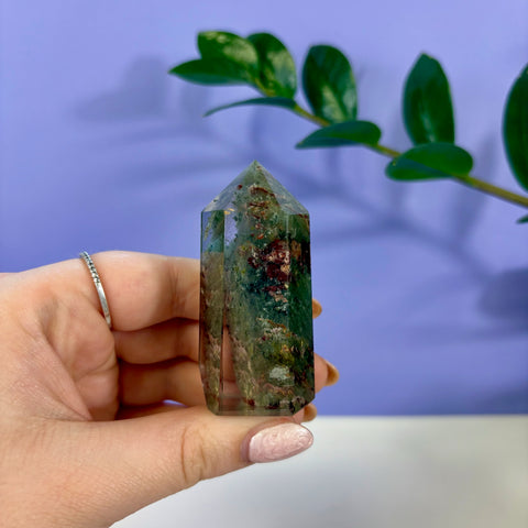Hand held garden quartz tower featuring green and earthy red mineral inclusions inside clear crystal.