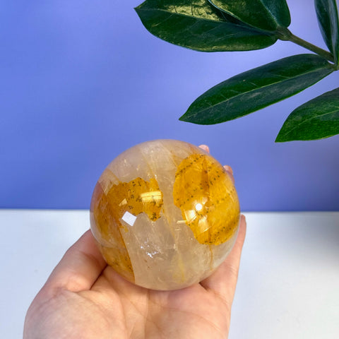 Hand holding a polished Girasol Golden Healer sphere with clear quartz and vibrant yellow-orange inclusions.