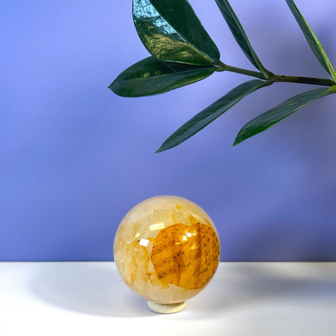 Girasol Golden Healer sphere with warm yellow and orange inclusions on a white stand, purple background.