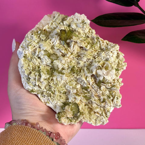 Hand holding a large, rough green tourmaline specimen with white matrix.
