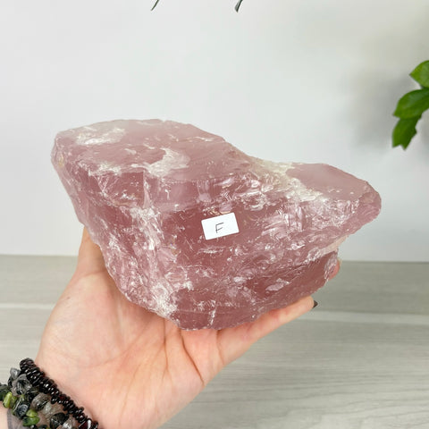 Large, rough-cut chunk of translucent pale pink rose quartz held in a hand against a white background.