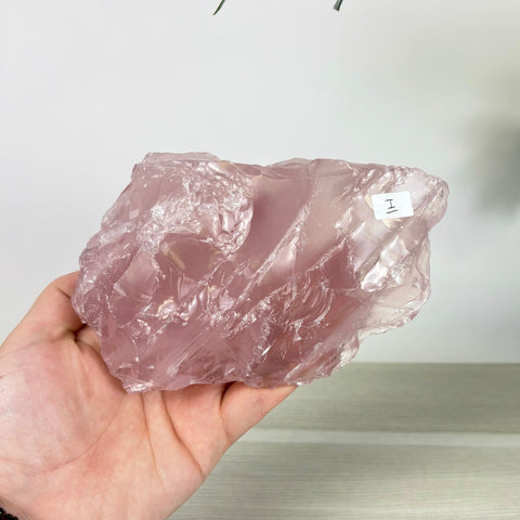 Large, translucent rose quartz chunk with a raw, crystalline texture held in a hand against a white background.