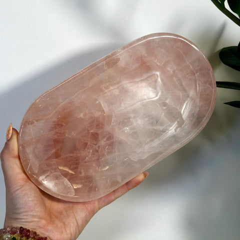 Hand holding an oval, polished, imperfect rose quartz plate with natural pink hues and inclusions.