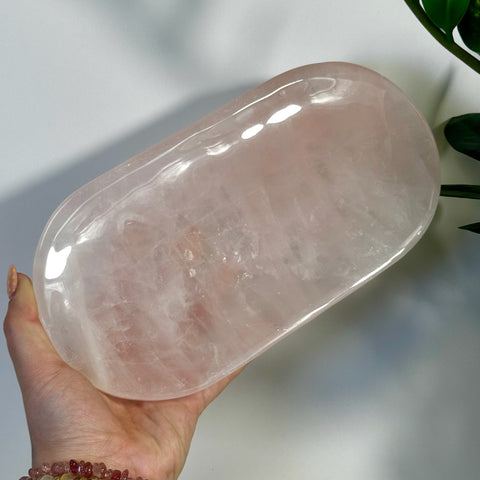 Hand holding a polished, imperfect rose quartz plate with a smooth, light pink surface.