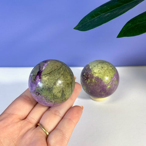 Hand holding an imperfect stichtite sphere, displaying vibrant purple and olive green hues.