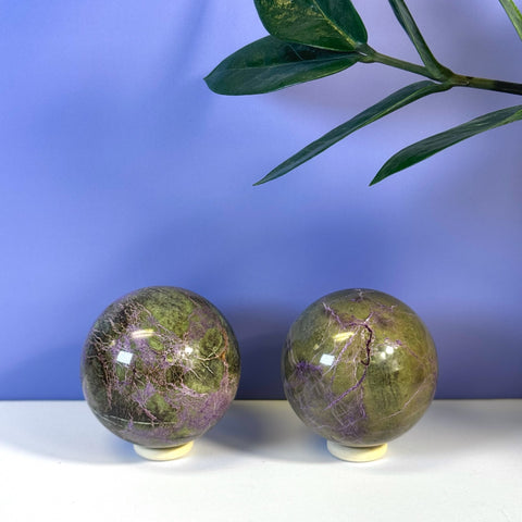 Two imperfect stichtite spheres, green with striking purple veins, on a white surface.