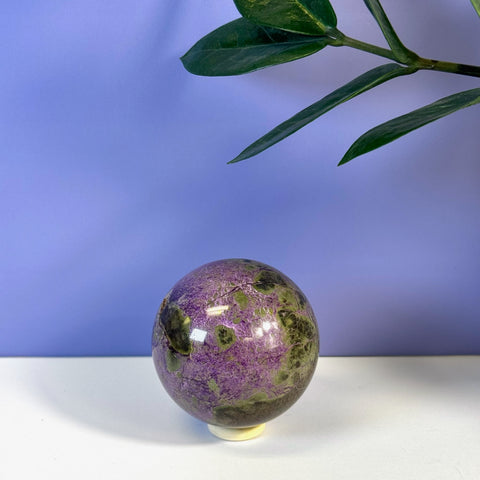 Glossy purple and green imperfect stichtite sphere on a white stand.