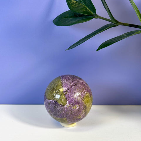 Imperfect stichtite sphere with mottled purple and olive green colors on a white stand.